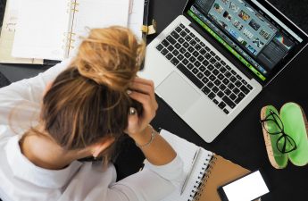 Overhead view of a stressed woman working at a desk with a laptop, phone, and notebooks.